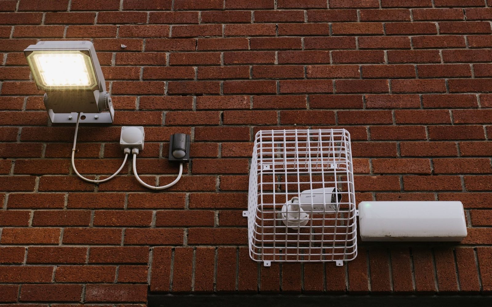 Security light, movement sensor and caged CCTV camera on a brick wall